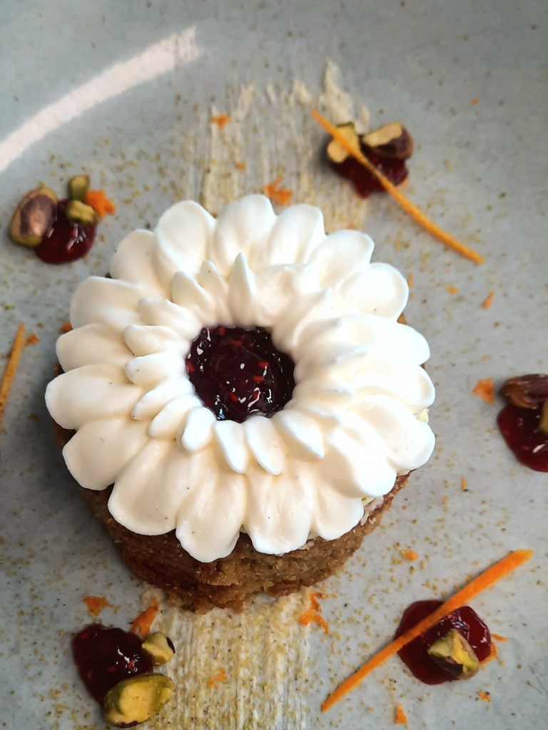 Whipped cream piped like petals on a round pistachio financier cake.