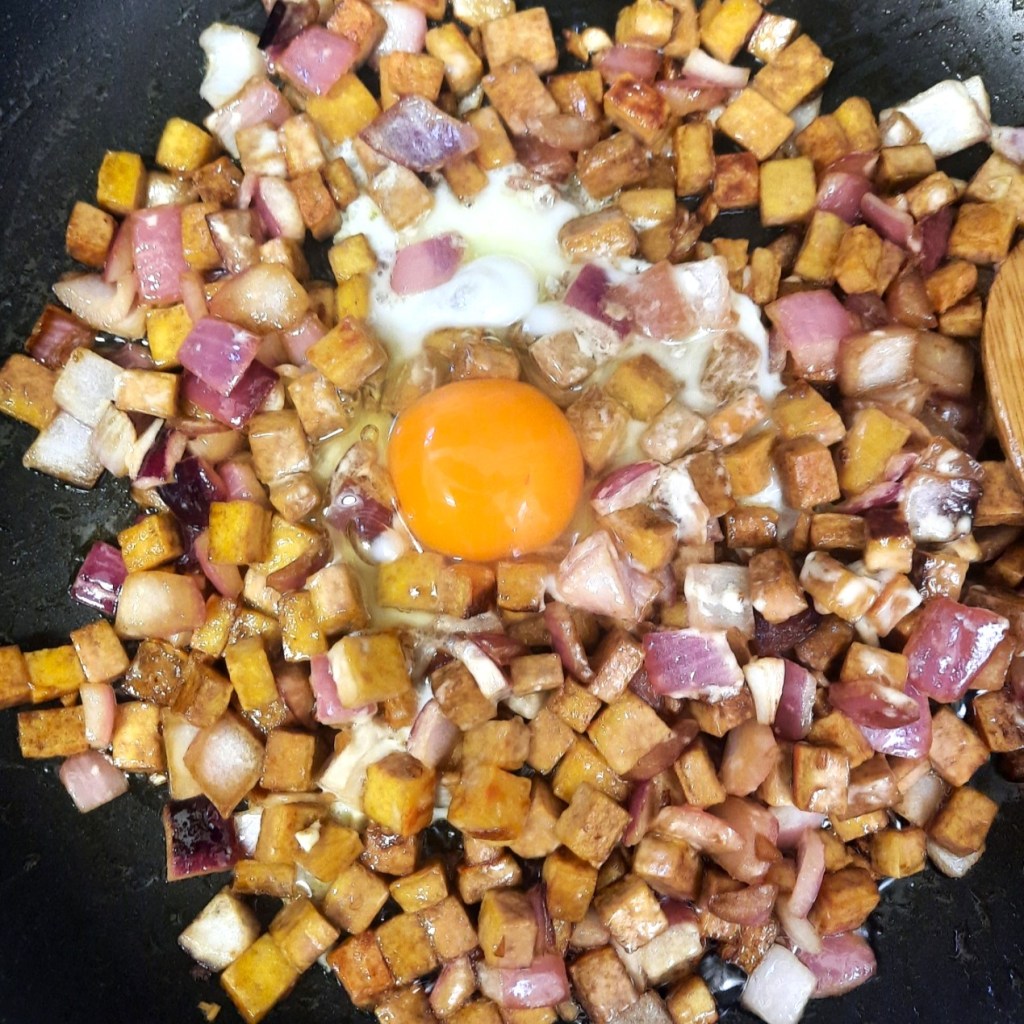 Quick Tofu Sisig with cracked raw egg on frying pan.